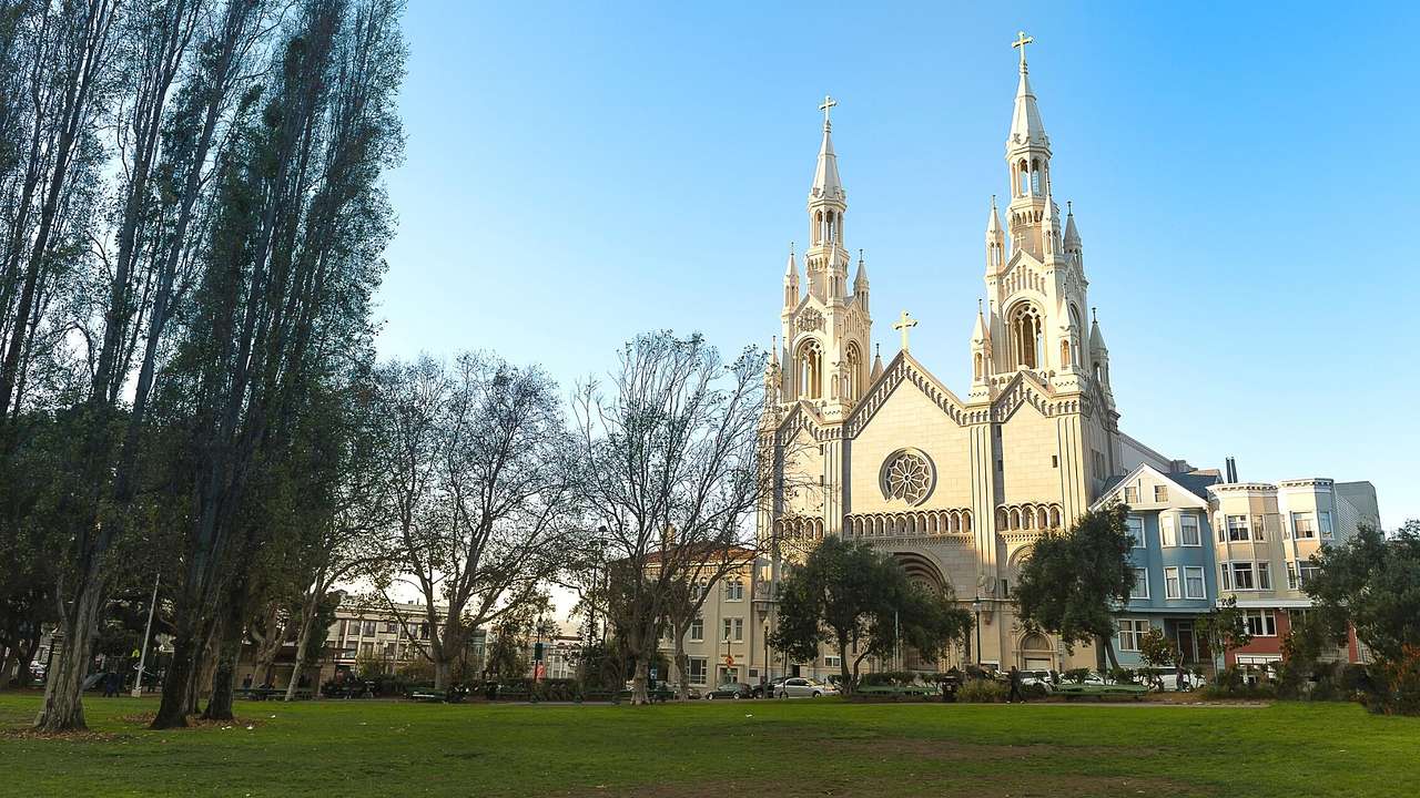 A cream-colored church with two steeples and grass and trees in front of it
