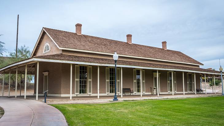 A walkway by green grass and an off white vernacular building with a brown roof