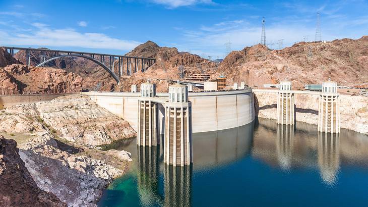 Water in a dam surrounded by rugged hills with an arched bypass bridge at the back