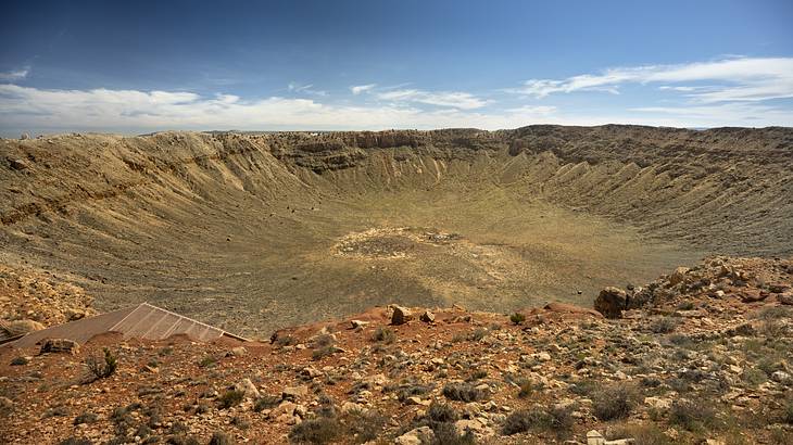 A round meteor impact site in a desert under a partly cloudy sky