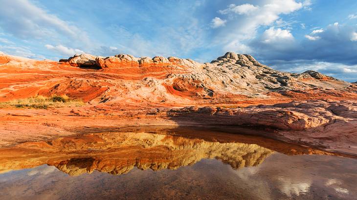 White-red sandstone cliffs with a water body in front under a partly cloudy sky