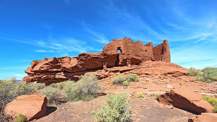 A rocky red sandstone hill with brick ruins under a partly cloudy sky