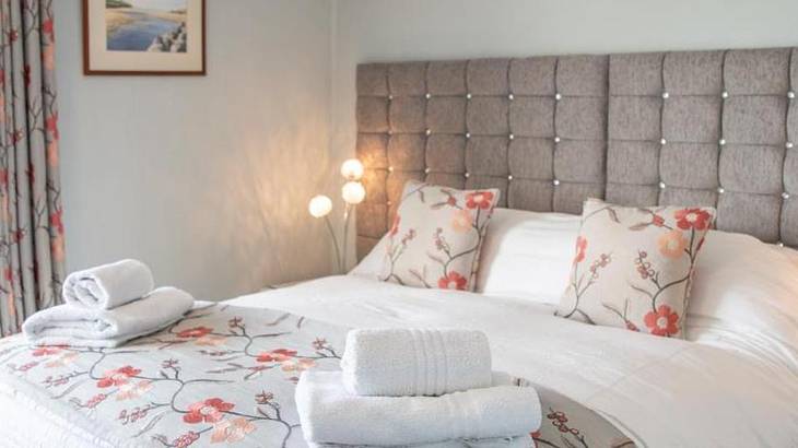 A bed with a grey headboard, floral pillows and blanket, and white towels on top