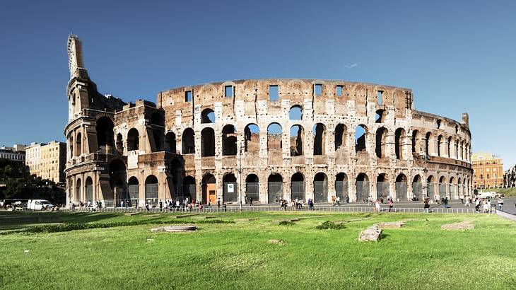 A panoramic shot of the Colosseum behind a large section of green grass, Rome, Italy
