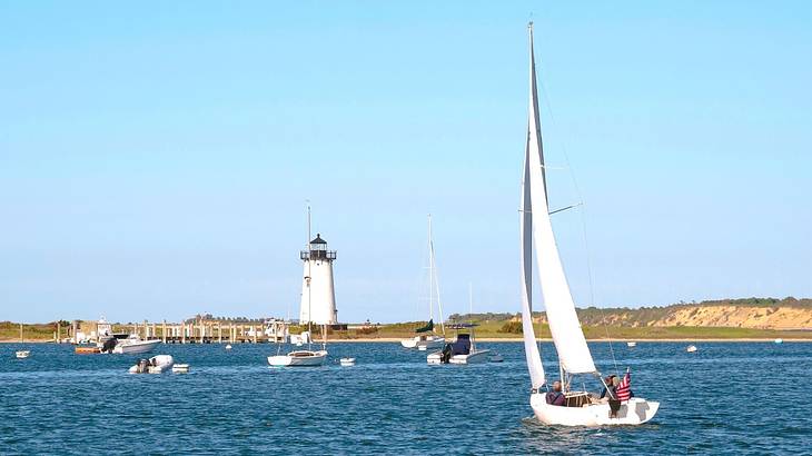 A sailboat on the water with a lighthouse and small cliffs in the distance