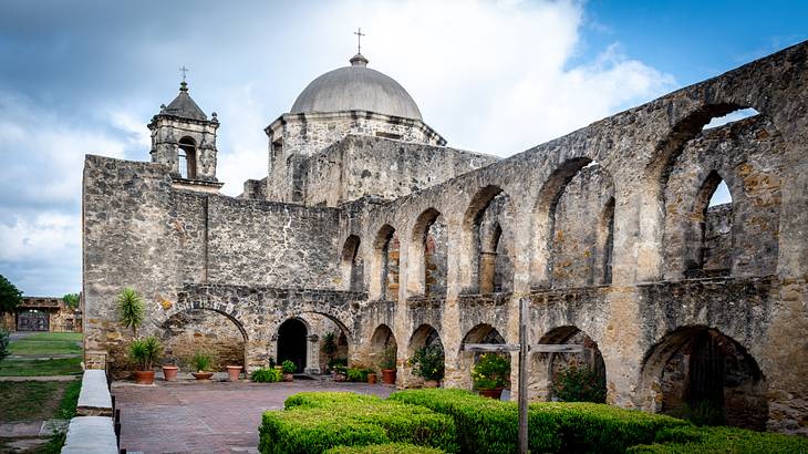 A park with stone arches connected to an archaic building with a cross on dome top