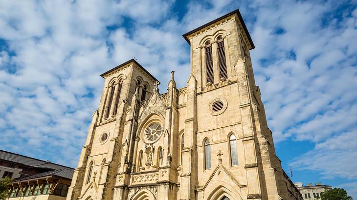 Looking up a gothic-style cathedral with cross on top against a partly cloudy sky