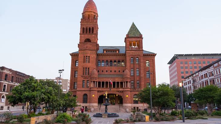 A Romanesque brown structure with two towers, a dark blue roof and a fountain outside