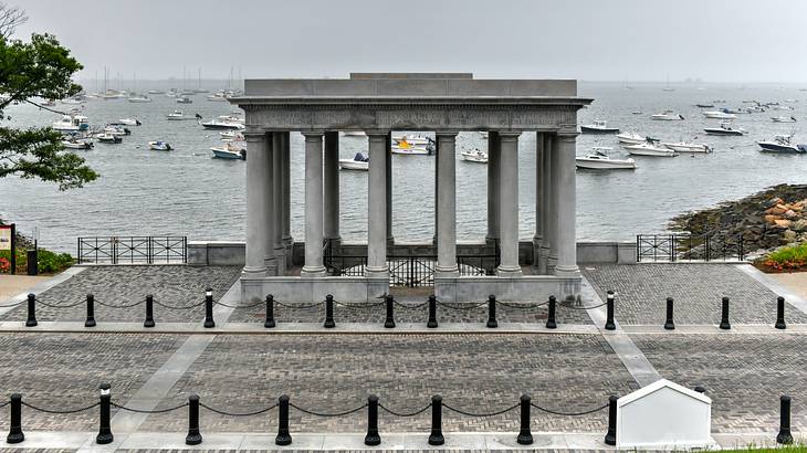 A gray neoclassical monument with columns against the water with white boats
