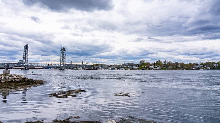 A body of water with rocks around and a city with clouds above in the background