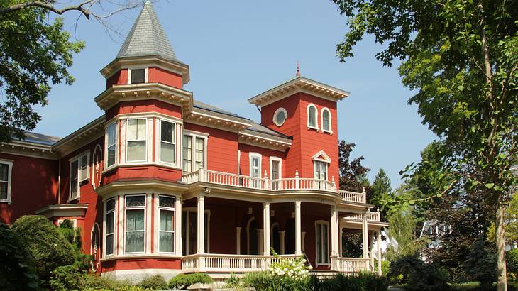 A large red victorian mansion with white shutters and a balcony and trees around