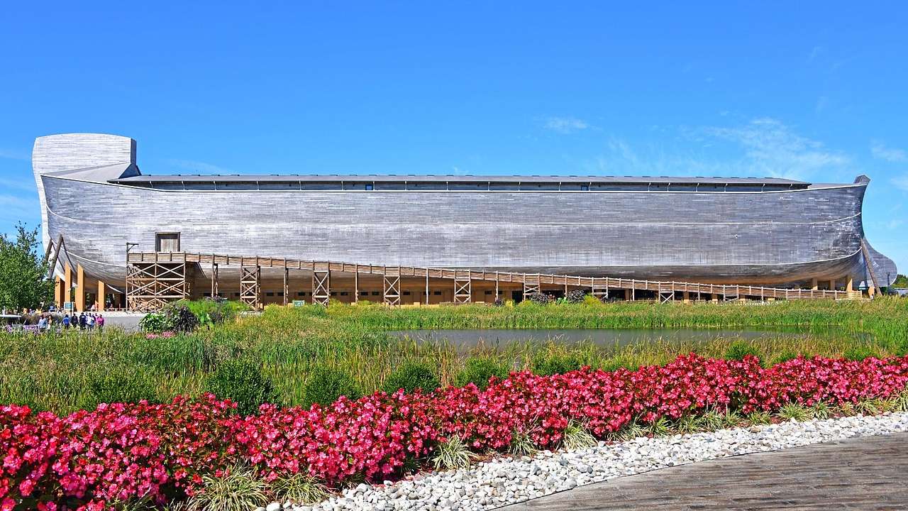 Red flowers and shrubs against a giant gray boat-shaped structure