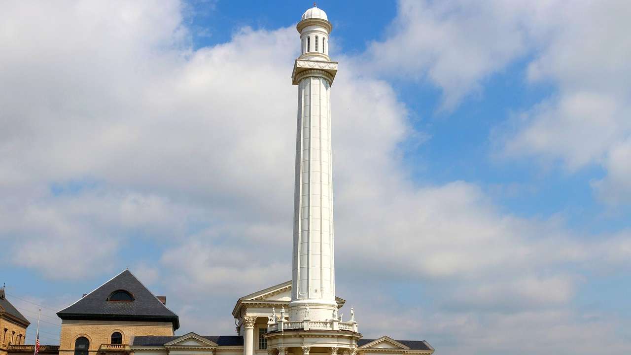A tall white tower next to a neoclassical building against a partly cloudy sky