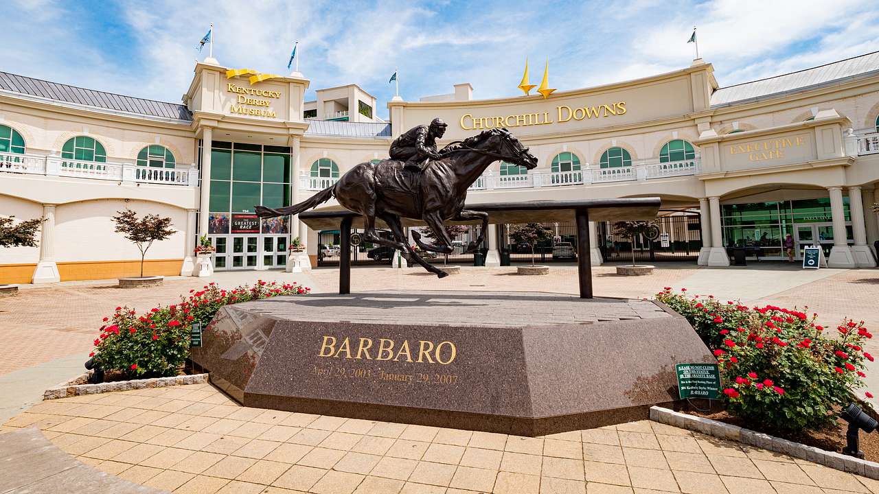 A black statue of a horse and jockey in front of a white building