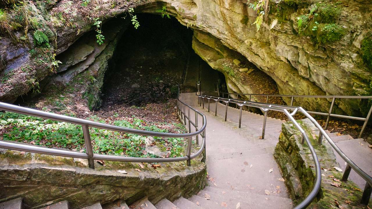 Stairs with metal railings leading down to the entrance of a cave