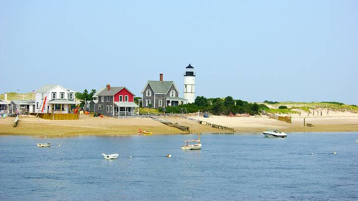 A lighthouse and small beach houses next to a sandy shore and the water