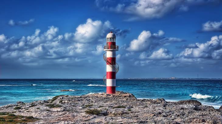 A red and white striped lighthouse standing on a rocky cliff by the blue sea