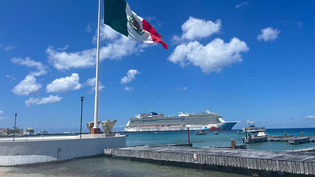A tall green, white, and red flag on a white platform with a cruise ship behind