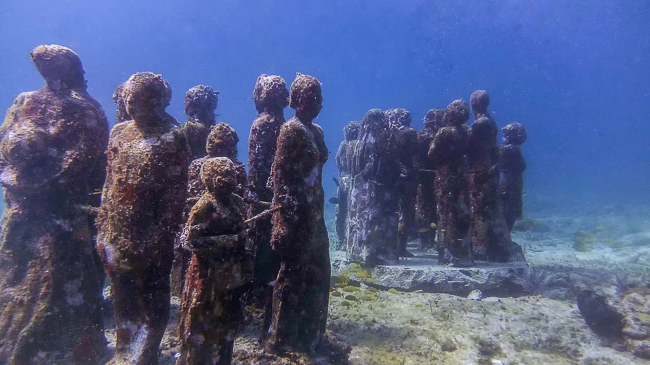 A group of statues under the water, covered in algae