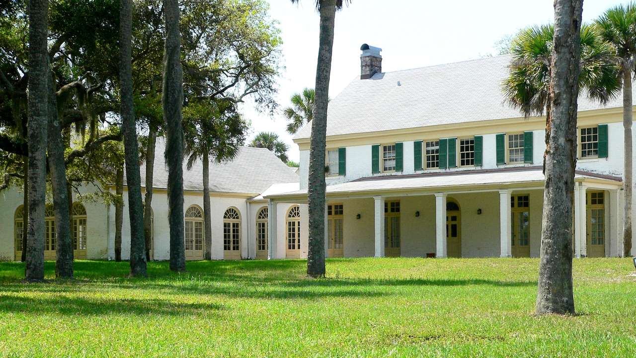A house with columns and green shutters next to green grass and palm trees