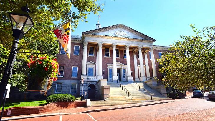 A historic building with columns and a triangular top, behind a road on a nice day