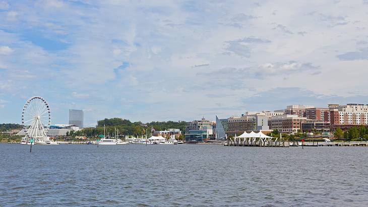 A river next to a city with buildings and a Ferris wheel under a blue sky with clouds