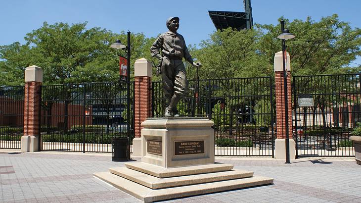 A statue of baseball player Babe Ruth next to trees and a fence