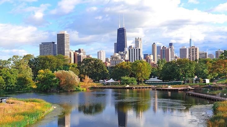 A lake with trees around it next to a city skyline under a cloudy sky