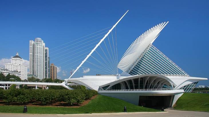 A contemporary white structure with greenery around it and tall buildings next to it