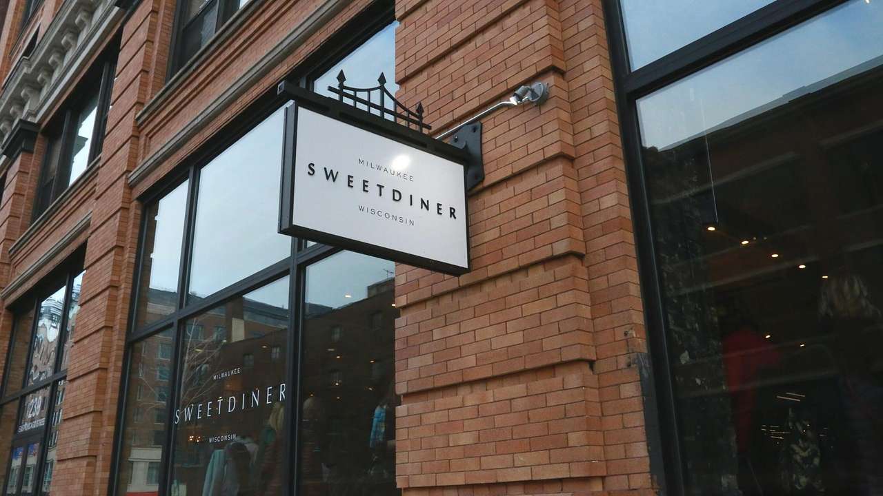 A brick building with windows and a white sign that says "Sweet Diner"