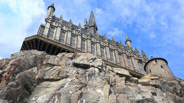 View from below of a castle on top of a rocky cliff, with blue sky in the background