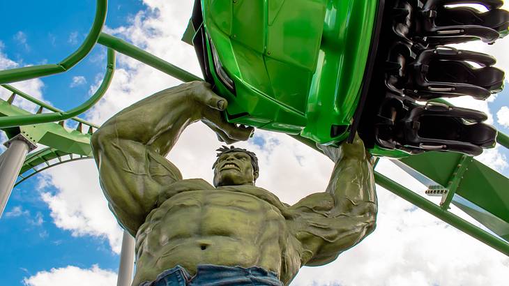 View from below of a green man statue lifting a green roller coaster car