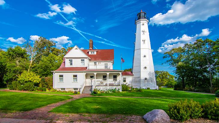 A white lighthouse beside a house on a bright cloudy day