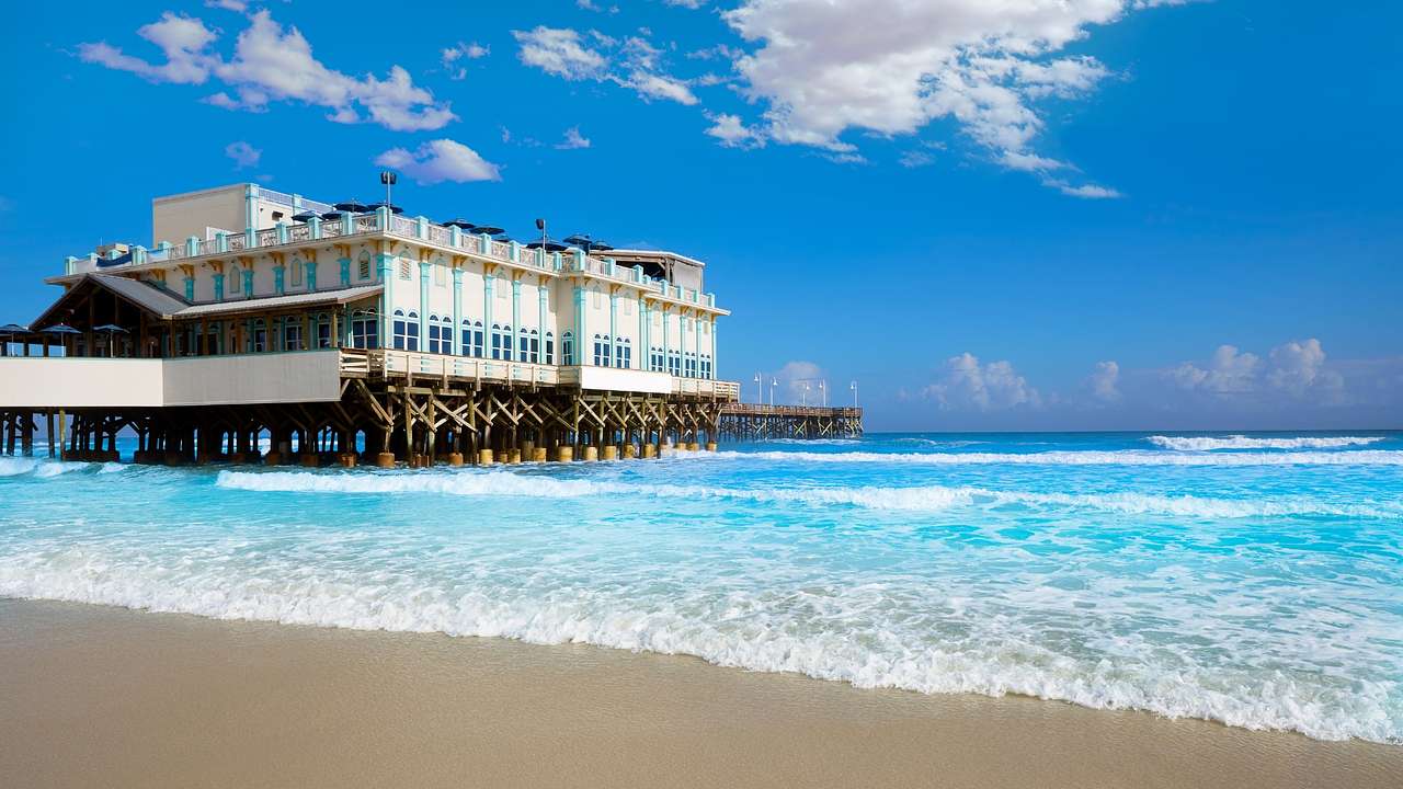 A large building on a pier next to bright blue water and a sandy beach