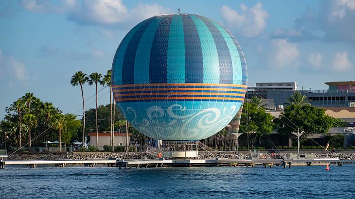 A blue hot air balloon tied on a pier, with buildings and trees in the background