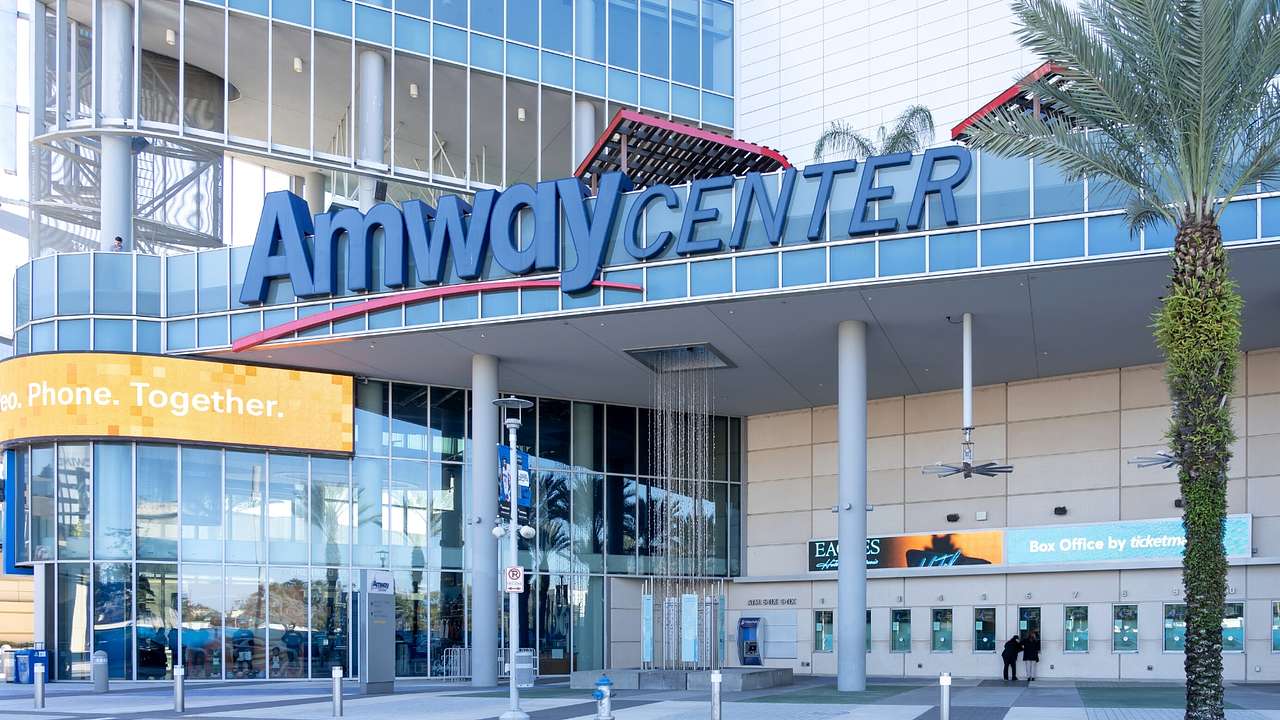 A stadium with glass windows and an "Amway Center" sign next to a green palm tree