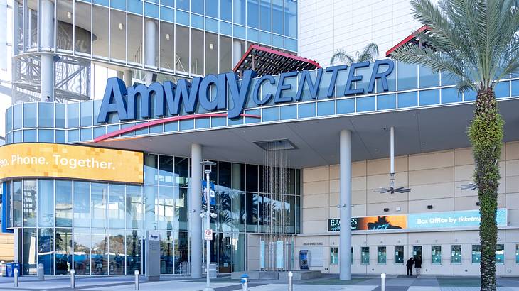 A stadium with glass windows and an "Amway Center" sign next to a green palm tree