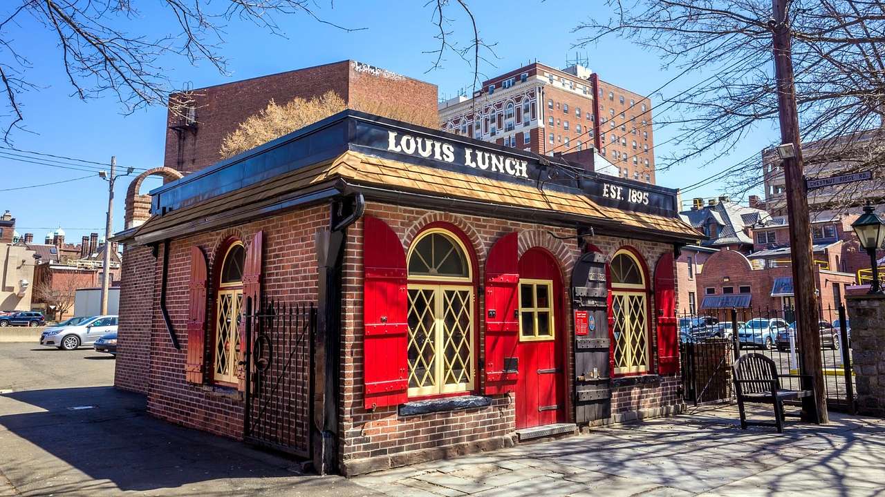 A red brick restaurant with a red door and a sign that reads "Louis Lunch"