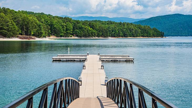 Lake with a small wooden pier and mountains and forest in the distance