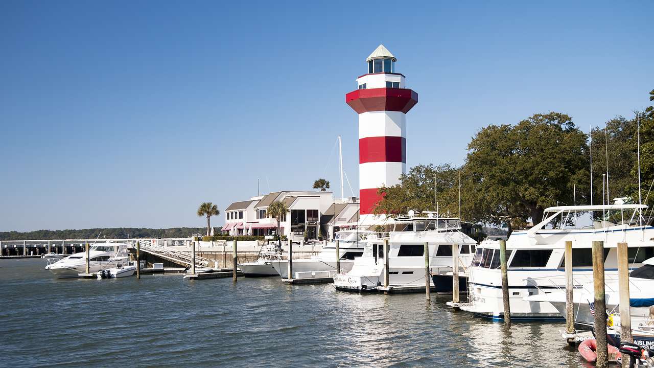 White and red striped lighthouse with white yachts docked in a pier