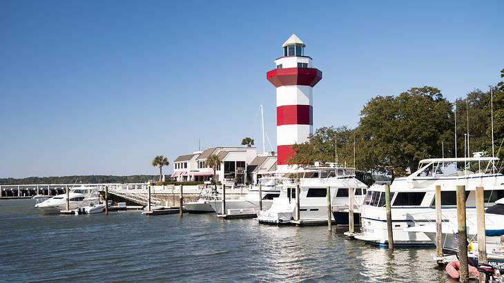 White and red striped lighthouse with white yachts docked in a pier