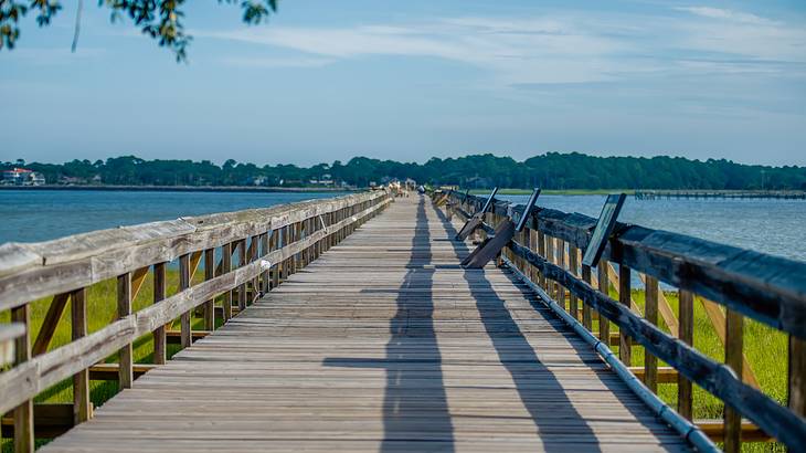 Long wooden boardwalk over water with green grass and blue sky around