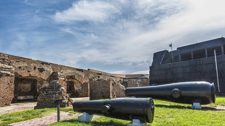 Old black cannons on green grass with ruins under a partly cloudy sky