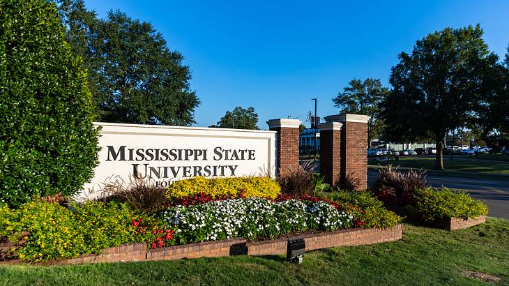 A signage that says Mississippi State University surrounded by flowers and trees