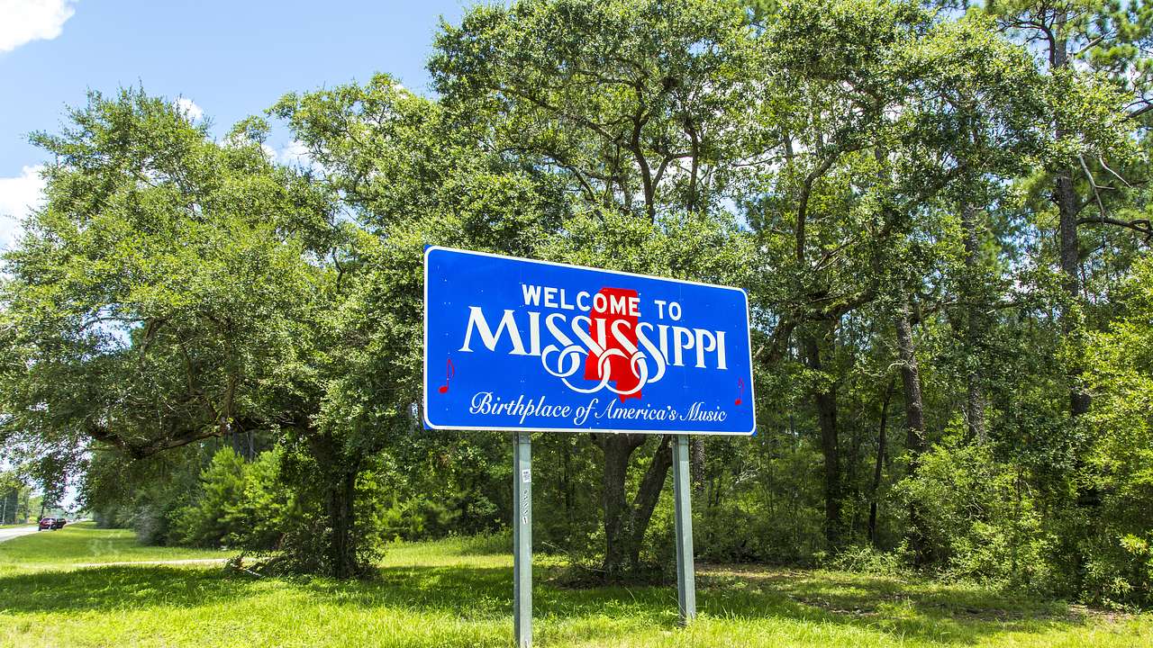 A white, blue, and red sign that says Welcome to Mississippi surrounded by greenery