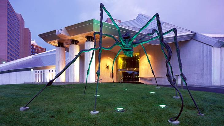 A spider sculpture in front of an illuminated museum at dusk