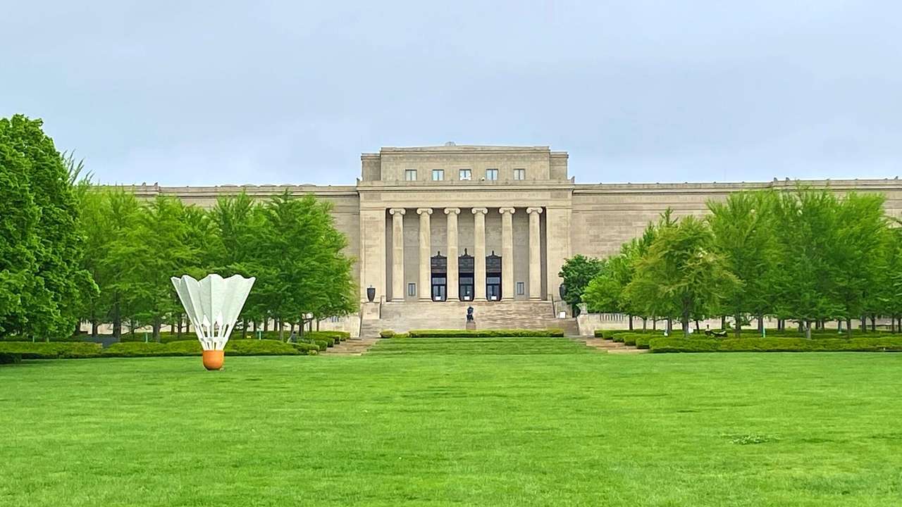 A stone museum with columns and a lawn in front of it with a shuttlecock sculpture