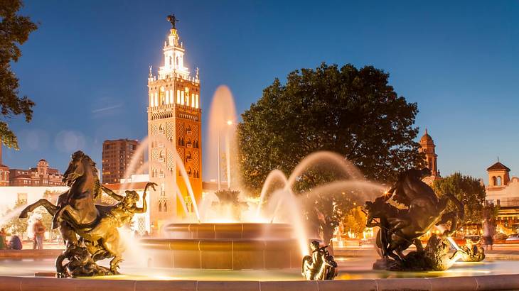 A water fountain with a tower behind it illuminated at night