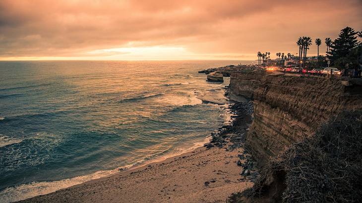 A cliff with trees on it next to the ocean at sunset