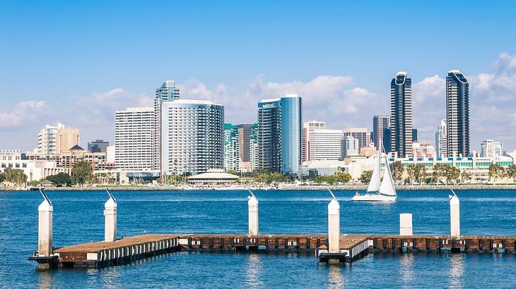 A bay with a boat dock and a sailboat on the water in front of city buildings